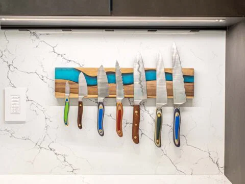 Studio 250 Design presents a set of six kitchen knives with colorful handles, magnetically mounted on a marble-style backsplash.