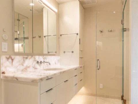 Discover a modern bathroom crafted by Studio 250 Design, where beige tones blend seamlessly with a large mirror, double sink with marble countertop, glass shower door, and recessed lighting. This space is the epitome of lifestyle-driven architecture.