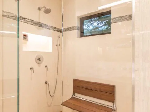 Experience the epitome of Wyoming Home Design with this modern shower. It features a sleek glass door, wooden bench, and slatted wooden floor. Enjoy the luxurious rainfall and handheld showerheads, complemented by a thoughtfully placed small window for natural light.