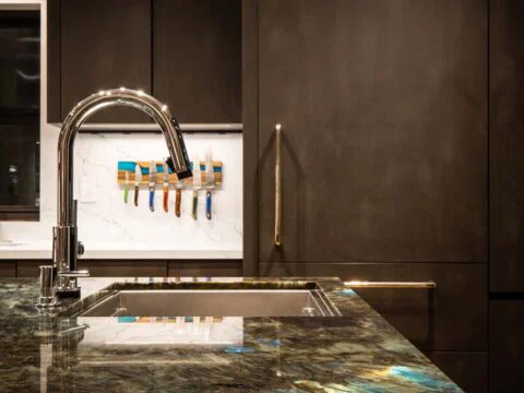 Modern kitchen with dark cabinetry, a sleek chrome faucet, and a colorful backsplash featuring hanging utensils. This Wyoming Home Design showcases personalized architecture that seamlessly blends style with functionality for the discerning homeowner.
