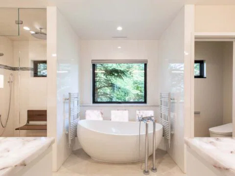 Modern bathroom by Studio 250 Design features a freestanding tub, large window, glass-enclosed shower, and dual vanities. Emphasizing light tones and minimalist elements, this lifestyle-driven architecture creates a serene retreat tailored to your everyday needs.